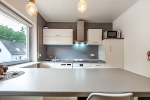 Eine moderne Küche mit einer großen Kochinsel, eingebauten Geräten und Pendelleuchten.