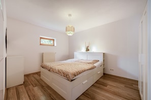 Ein Schlafzimmer mit einem Bett, einem Schminktisch, einem Heizkörper, einem Fenster und einer Wandleuchte.