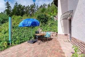 Eine Außenpatio mit Tisch, Stühlen, einem blauen Sonnenschirm und einem Pflasterweg.