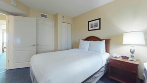Una habitación de hotel con una cama grande, una mesita de noche con lámpara y una puerta que da a otra habitación.