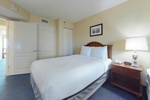 Ein Hotelzimmer mit einem großen Bett, einem Nachttisch mit einer Lampe und einer Tür zu einem anderen Raum.