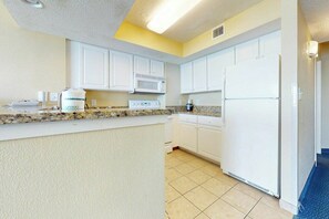 A kitchen with white cabinets, a microwave, a stove, and a refrigerator. - Carolinian Beach Resort 1831 (Myrtle Beach)