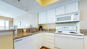 Una cocina compacta con armarios blancos, microondas, estufa y lavavajillas.