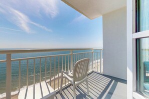 A balcony with a view of the ocean, a white chair, and a window.