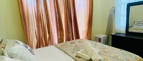 Una habitación de hotel con cama, cortinas, un escritorio con espejo y un ventilador de techo.