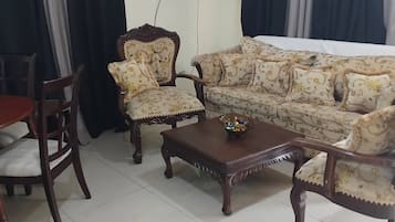 A living room with a sofa, two armchairs, a coffee table, a TV, and curtains.