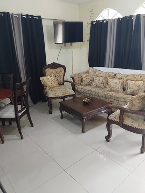 A living room with a sofa, two armchairs, a coffee table, a TV, and curtains. - Paris London House in Samana (Samaná)