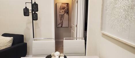 A dining area with a table, chairs, a bowl of decorative items, a black pendant light, and a wall with a textured pattern.