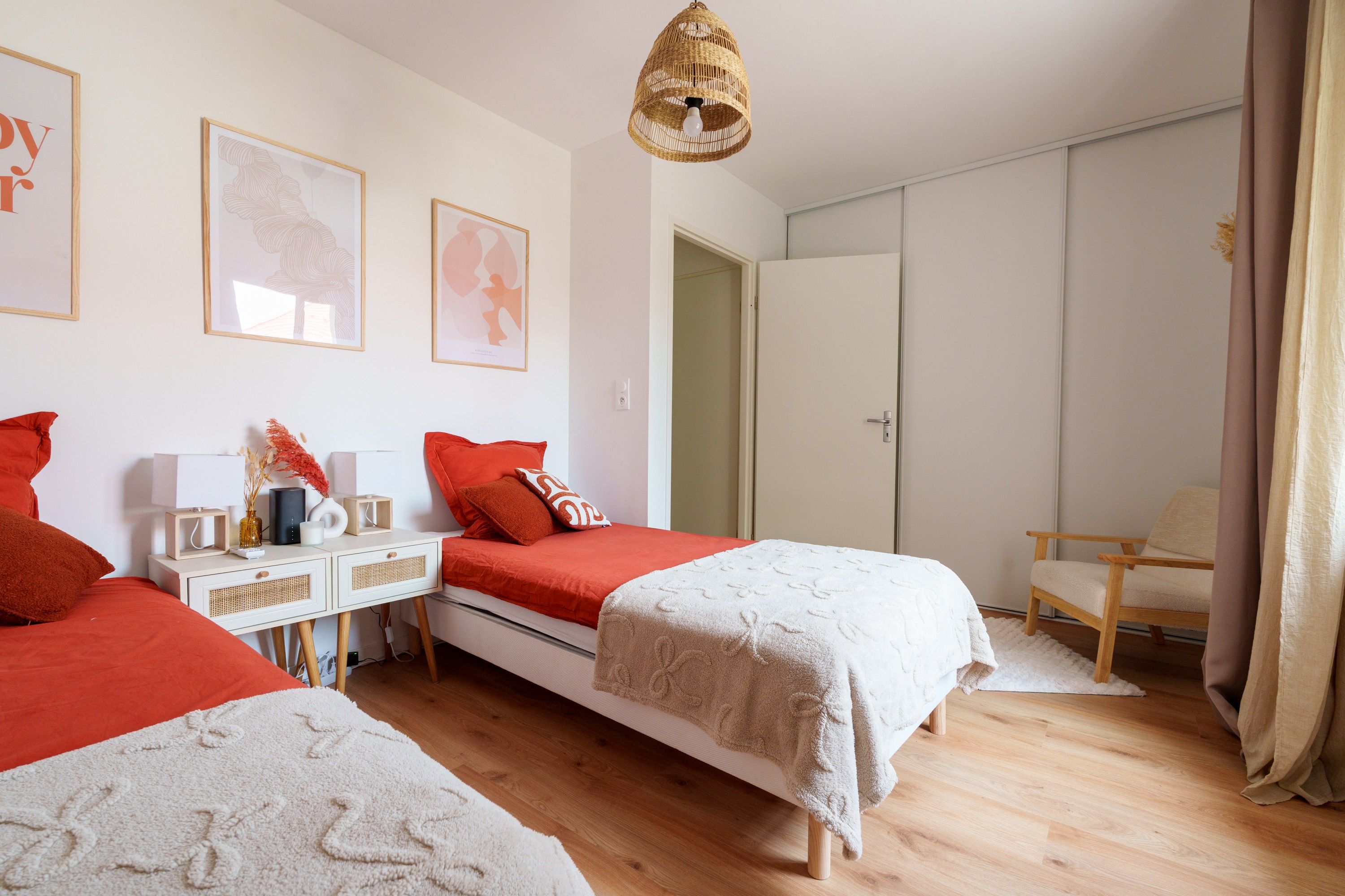 Une chambre avec deux lits, une table de chevet, une chaise, une armoire et un luminaire suspendu.
