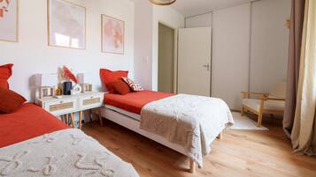 Une chambre avec deux lits, une table de chevet, une chaise, une armoire et un luminaire suspendu.