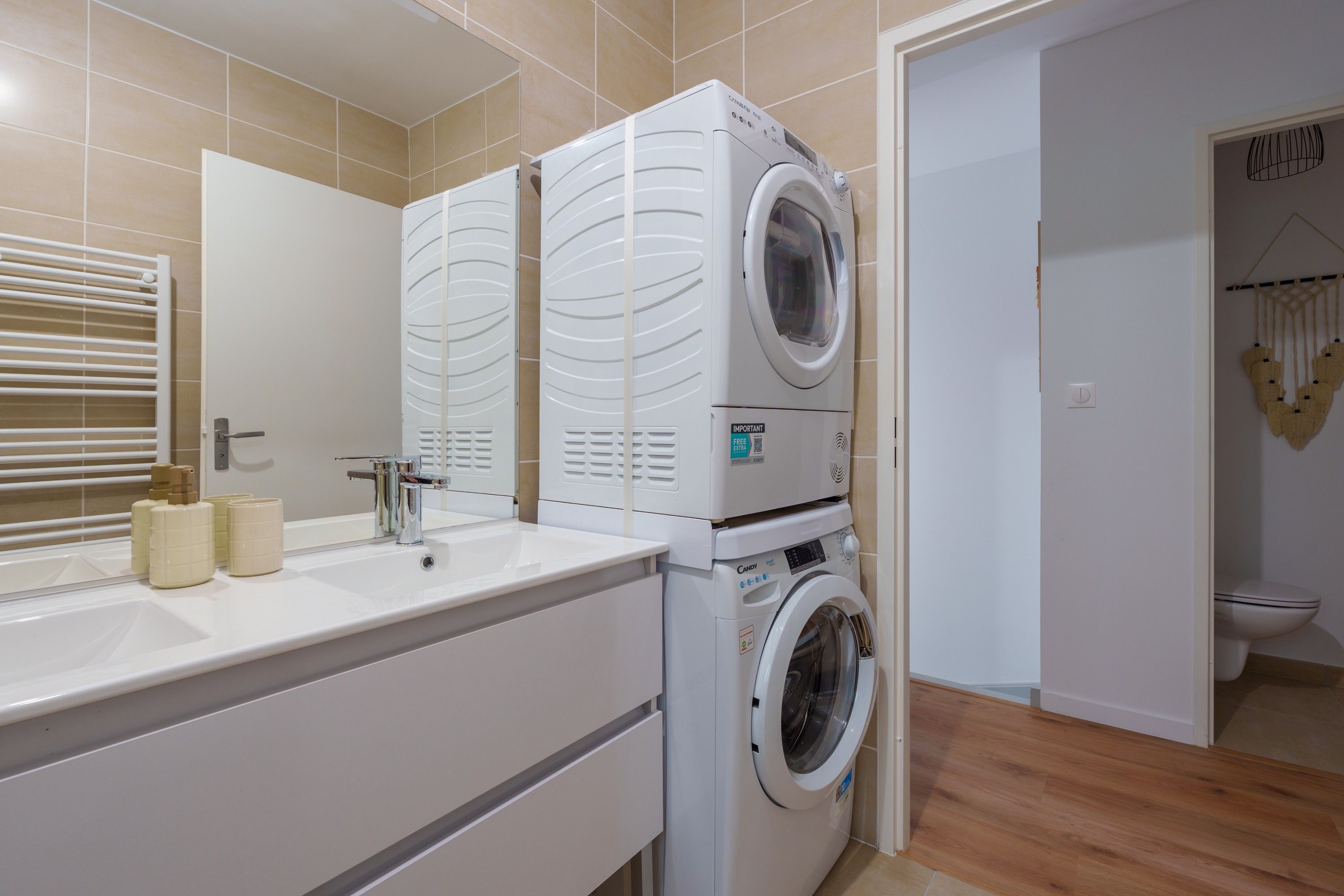 Een moderne badkamer met een wasmachine en droger, een wastafel met toiletartikelen en een spiegel.