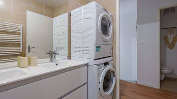 Een moderne badkamer met een wasmachine en droger, een wastafel met toiletartikelen en een spiegel.
