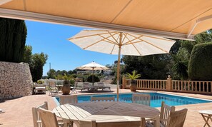 A pool area with a table and chairs, a large umbrella, and a stone wall. - Villa in Benissa with private pool for 8 guests | Costa Blanca holiday rental - ALELUYA (Benissa)
