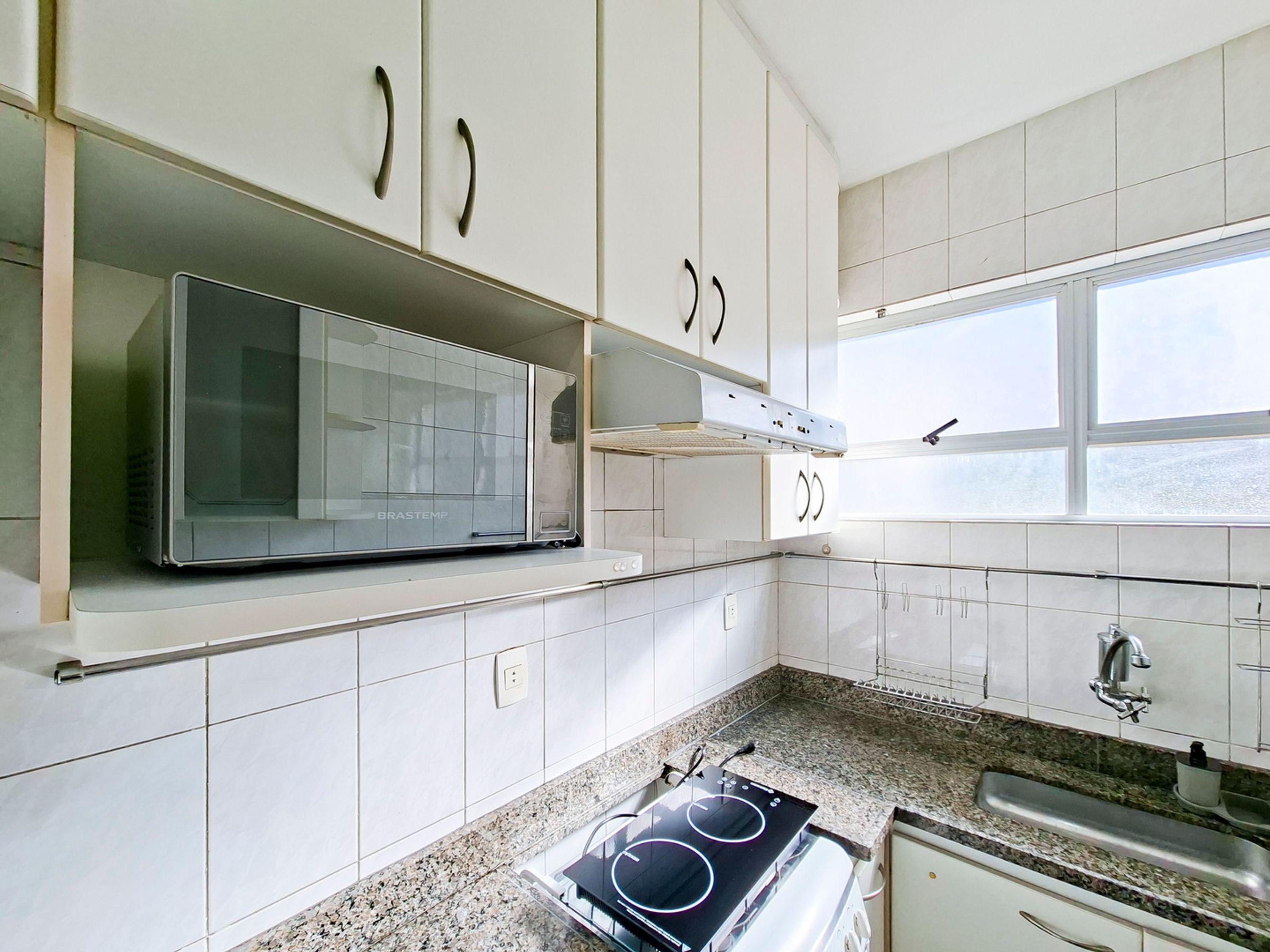 A kitchen with white cabinets, a microwave, a stove, and a window.