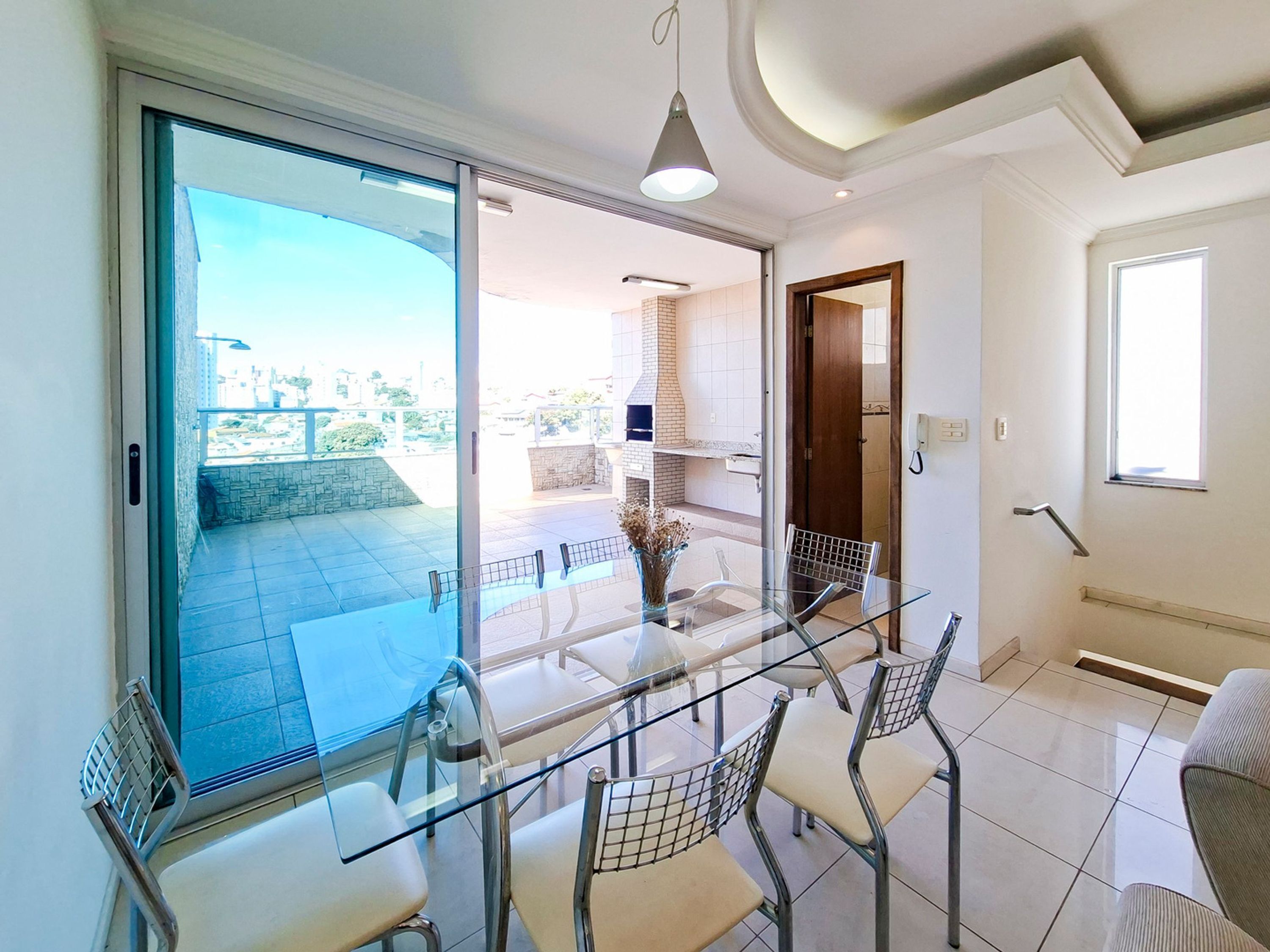 A modern interior with a glass dining table, chairs, and a view of the outdoor terrace.