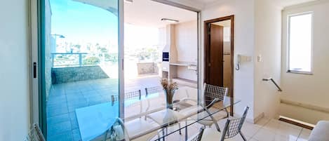 Un interior moderno con una mesa de comedor de cristal, sillas y vistas a la terraza exterior.