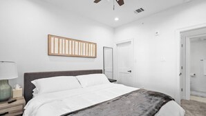 Ein Schlafzimmer mit einem Bett, einem Nachttisch, einer Lampe und einer Tür.