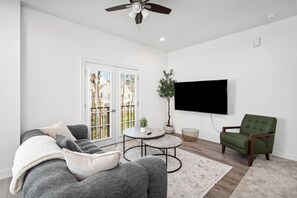 A living room with a sofa, armchair, coffee table, and a flat-screen TV mounted on the wall. - Newly Built: C: 1BR/1BA/Modern Condo in Houston (Houston)