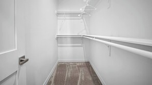 Ein schmaler Korridor mit Teppichboden, einer Tür links und einer weißen Wand mit einer Leuchte und einem Regal rechts.
