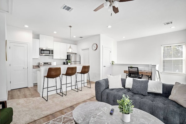 Una cocina moderna con armarios blancos, microondas y un comedor con mesa y sillas.