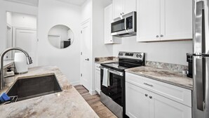 A modern kitchen with white cabinetry, a stainless steel refrigerator, a built-in oven, and a microwave.