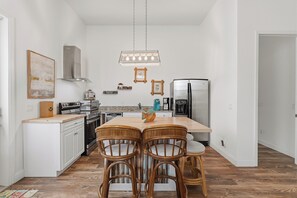 A kitchen with white cabinets, a wooden dining table, and four wicker chairs. - 🌊Tranquil Tides | Hill St Beach House Just Steps from the Sand🏖️ (New Smyrna Beach)