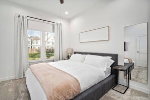 Ein Schlafzimmer mit Bett, Nachttischen, einem Fenster mit Vorhängen, einem Wandbild und einer Tür.