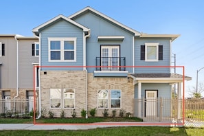 A two-story residential building with a balcony, a garage, and a fenced yard. - New Build: D: 1BR/1BA Modern Condo in Houston (Houston)