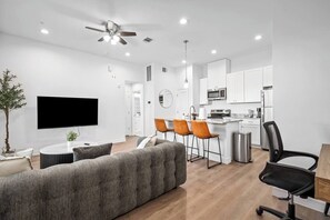 A modern living room with a flat-screen TV, a sofa, and a dining area with chairs. - New Build: D: 1BR/1BA Modern Condo in Houston (Houston)