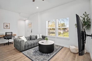 Ein modernes Wohnzimmer mit einem grauen Sofa, einem runden Couchtisch und einem Fernseher.