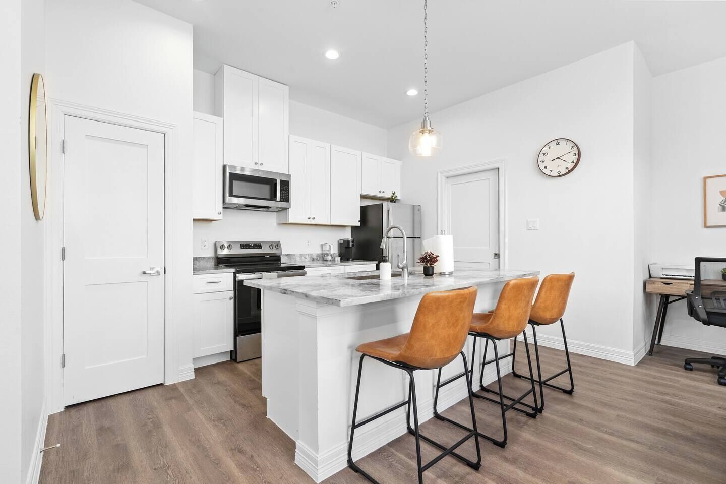 A modern kitchen with white cabinetry, a central island with bar stools, a microwave, a stove, and a sink.