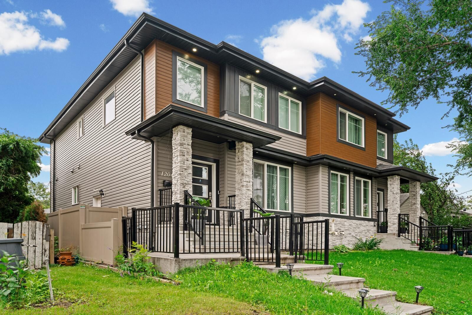 A two-story house with a stone column, a wooden front porch, and a black railing.