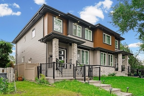 A two-story house with a stone column, a wooden front porch, and a black railing. - 
Stylish 4BR 5Bed Oasis | Fast Wi-Fi & Free Parking (Edmonton)