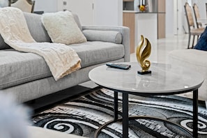 A living room with a grey sofa, a round coffee table with a remote control and a decorative item, and a patterned rug. - 
Stylish 4BR 5Bed Oasis | Fast Wi-Fi & Free Parking (Edmonton)