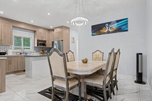 A modern kitchen with wooden cabinets, a refrigerator, and a dining area with a marble table and upholstered chairs. - 
Stylish 4BR 5Bed Oasis | Fast Wi-Fi & Free Parking (Edmonton)
