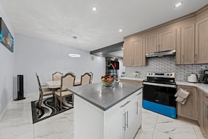 A modern kitchen with a central island, wooden cabinets, a built-in oven, and a dining area with a table and chairs. - 
Stylish 4BR 5Bed Oasis | Fast Wi-Fi & Free Parking (Edmonton)