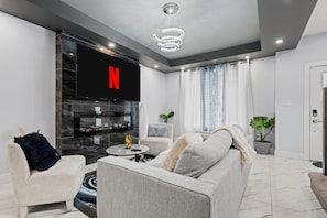 A modern living room with a flat-screen TV, a fireplace, and a coffee table. - 
Stylish 4BR 5Bed Oasis | Fast Wi-Fi & Free Parking (Edmonton)