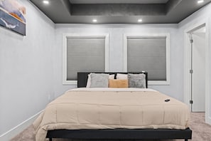 A bedroom with a bed, two windows with blinds, a door, and a ceiling light. - 
Stylish 4BR 5Bed Oasis | Fast Wi-Fi & Free Parking (Edmonton)
