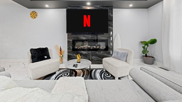 Un soggiorno moderno con una TV a schermo piatto montata su una parete in marmo nero, due divani bianchi, un tavolino rotondo con un oggetto decorativo e una pianta in vaso.