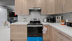 Una cucina moderna con mobili chiari in legno, un piano cottura nero e uno schienale rivestito di piastrelle bianche.