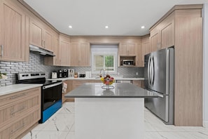A modern kitchen with wooden cabinets, a stainless steel refrigerator, and a central island. - 
Stylish 4BR 5Bed Oasis | Fast Wi-Fi & Free Parking (Edmonton)