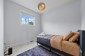 Ein Schlafzimmer mit einem Bett, einem Fenster, einer Heizung und einer Pendelleuchte.