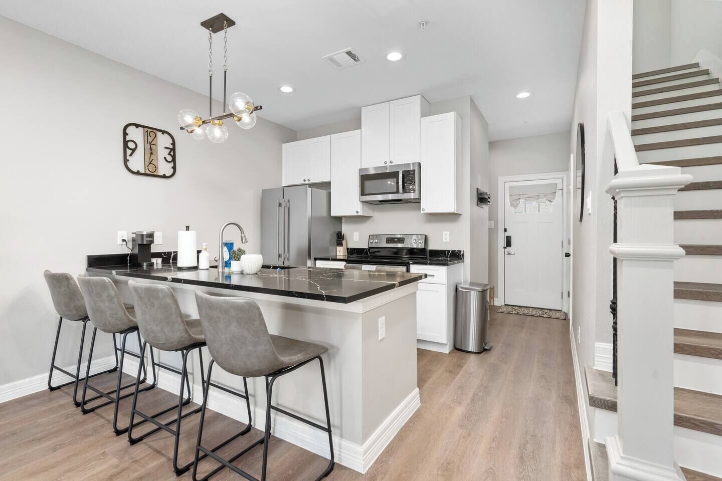 A modern kitchen with a central island, bar stools, stainless steel appliances, and a decorative clock.
