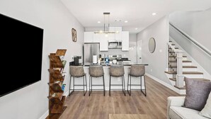A modern kitchen with a central island, bar stools, and a staircase to the right. - New Build 2-Story Townhome/Single Master Suite (Houston)