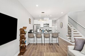 A modern kitchen with a central island, bar stools, and a staircase to the right. - New Build 2-Story Townhome/Single Master Suite (Houston)