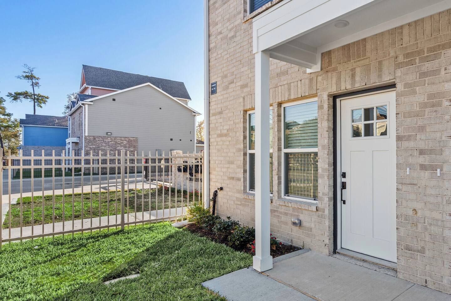 A residential building with a white door, a brick facade, and a small front yard with a white fence.