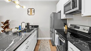 A modern kitchen with a black marble countertop, stainless steel appliances, and a unique wall clock. - New Build 2-Story Townhome/Single Master Suite (Houston)