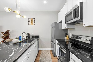 A modern kitchen with a black marble countertop, stainless steel appliances, and a unique wall clock. - New Build 2-Story Townhome/Single Master Suite (Houston)