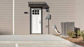 A building with a single door and a small window, a utility box, and a clear sky. - New Build 2-Story Townhome/Single Master Suite (Houston)