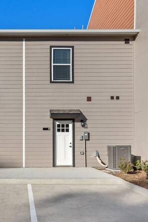 A building with a single door and a small window, a utility box, and a clear sky. - New Build 2-Story Townhome/Single Master Suite (Houston)